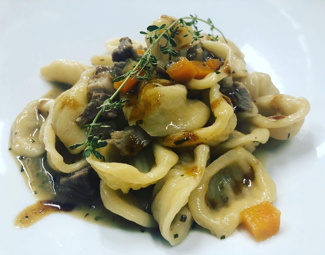 Pasta con funghi, verdure e guarnizione di erbe aromatiche su un piatto bianco.
