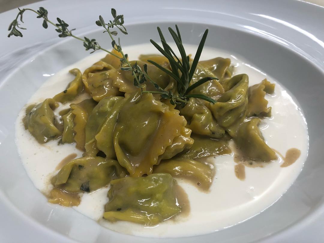Ravioli in salsa verde, guarniti con rosmarino e serviti su un piatto bianco.