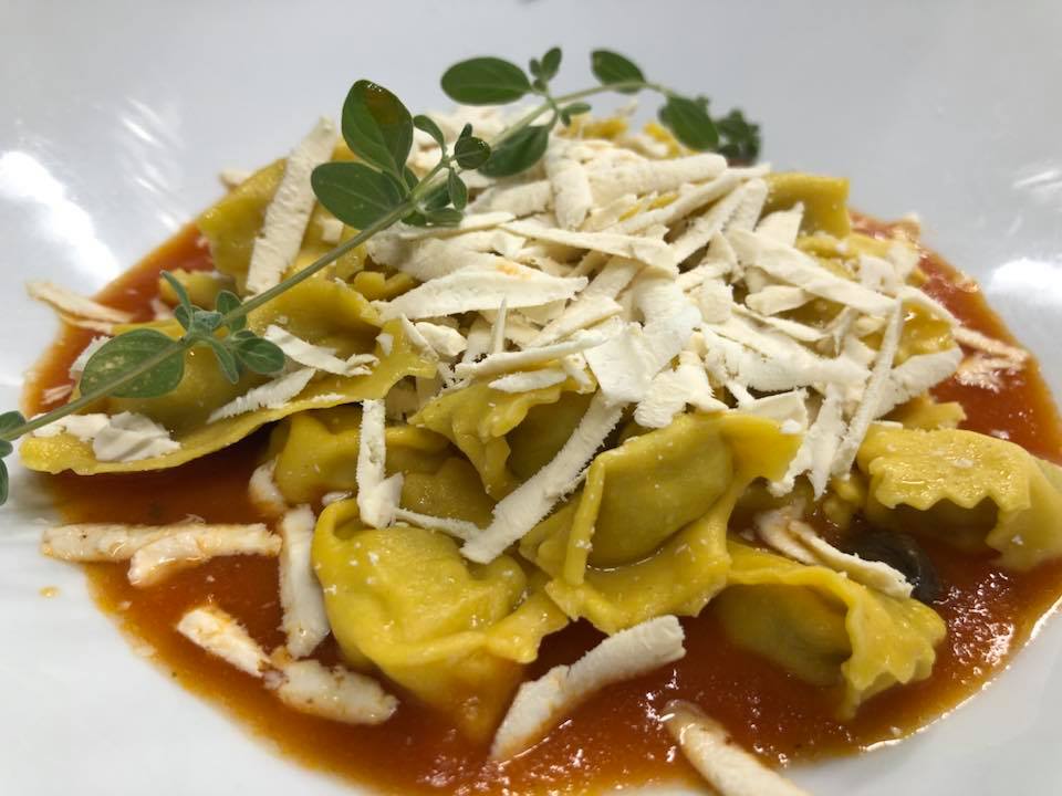 Ravioli al sugo di pomodoro con formaggio grattugiato e un rametto di basilico, serviti su un piatto bianco.
