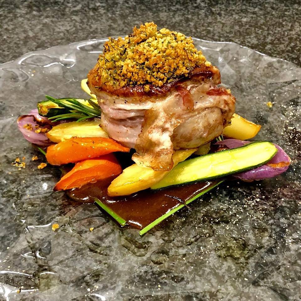 Carne scottata in crosta di erbe aromatiche, verdure colorate e salsa servite su un piatto di vetro.