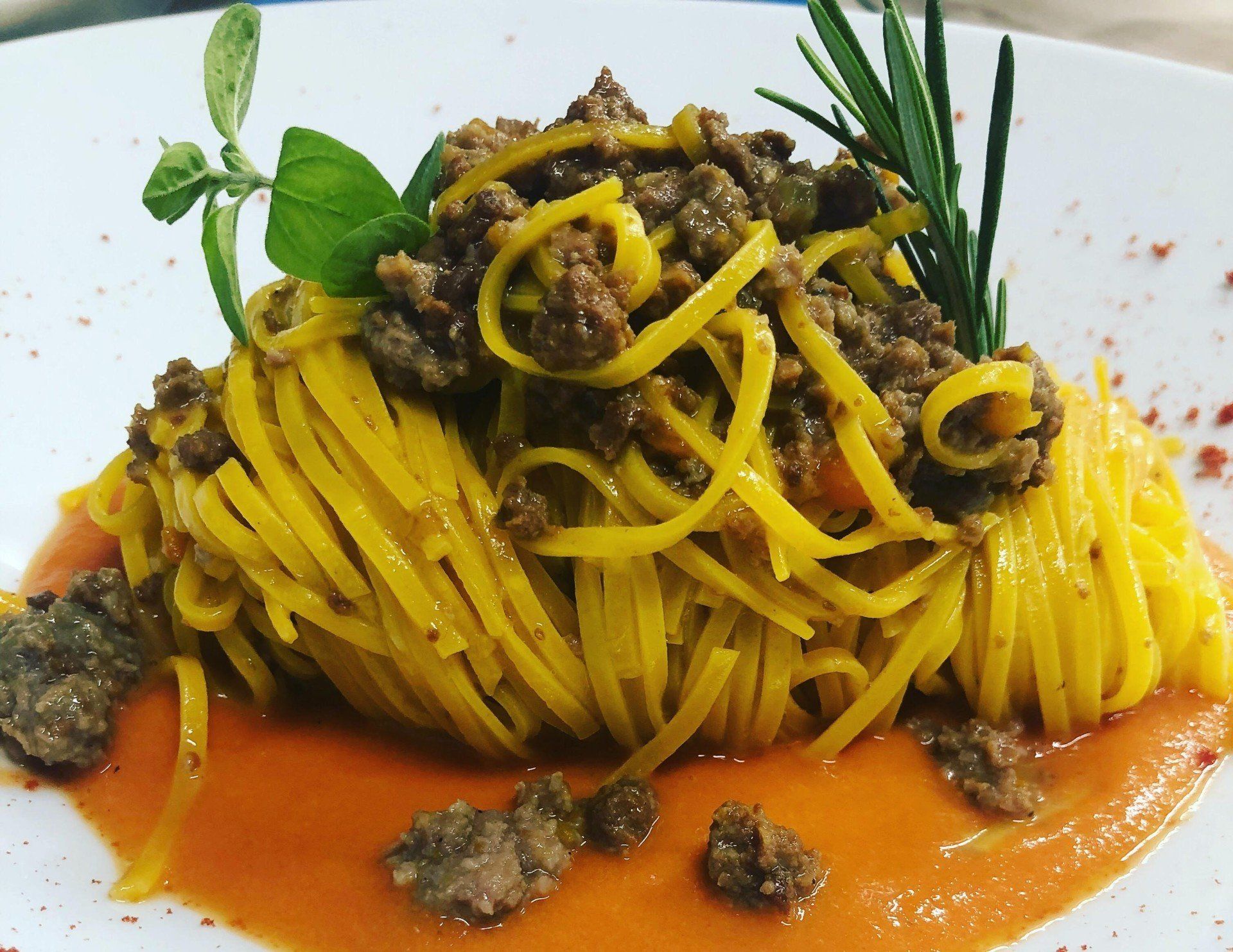 Pasta gialla al ragù su un piatto bianco, guarnita con erbe aromatiche e salsa all'arancia.
