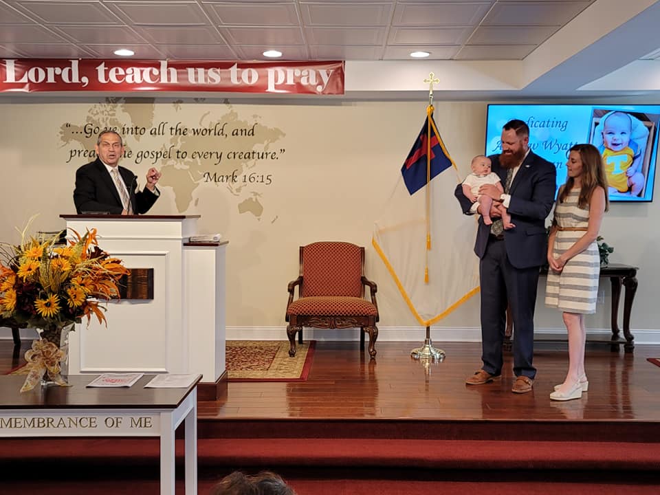 Church stage with speaker at podium and family standing beside a flag and screen.