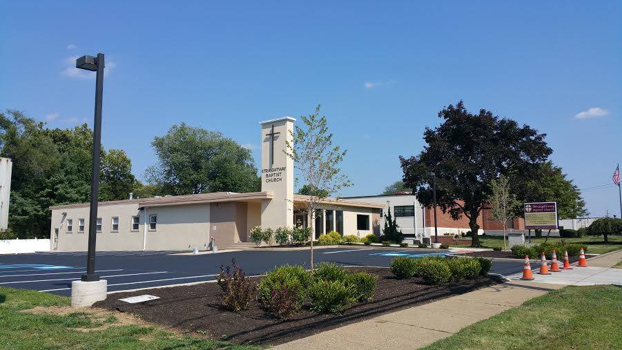 Modern building entrance with a tower, landscaped shrubs, and a sidewalk under a clear sky