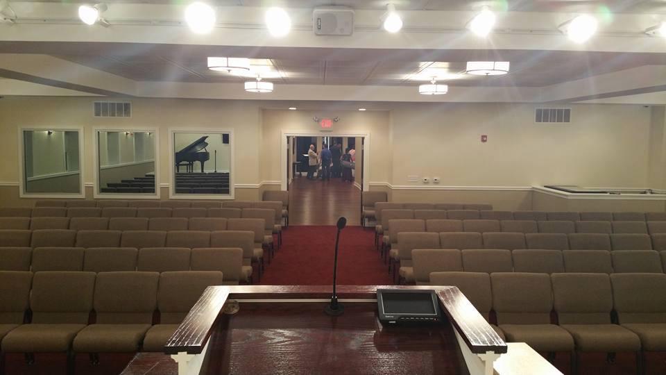 Empty auditorium with rows of tan seats, red carpet aisle, and stage viewed from the front.