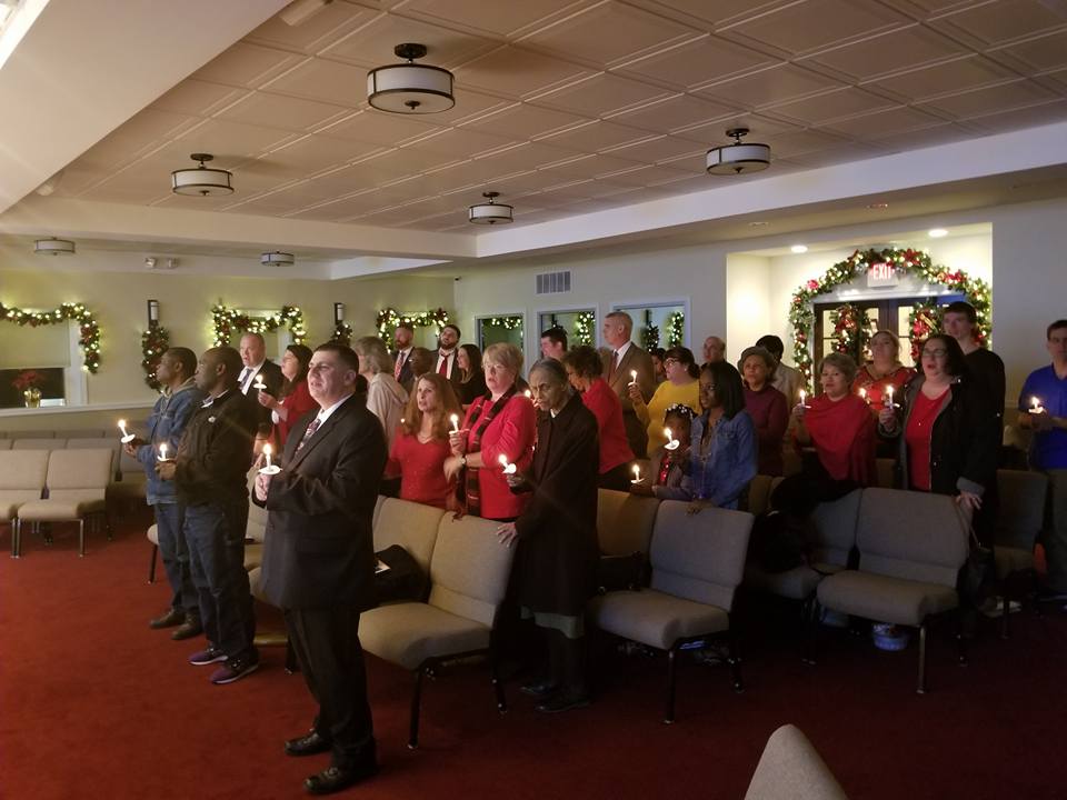 People standing and singing in a decorated hall during a holiday gathering.