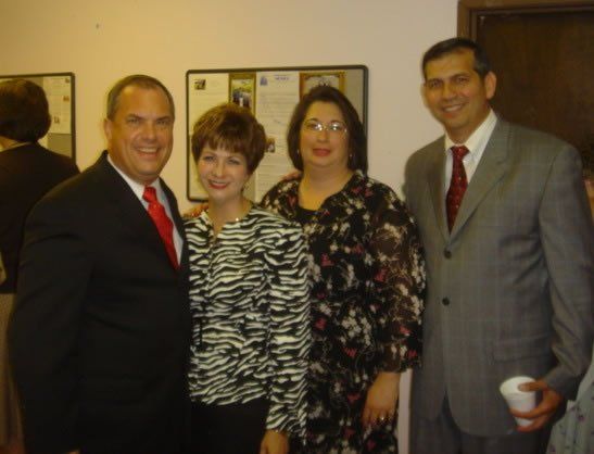 Four people posing indoors at a formal gathering, wearing business attire and smiling at the camera.