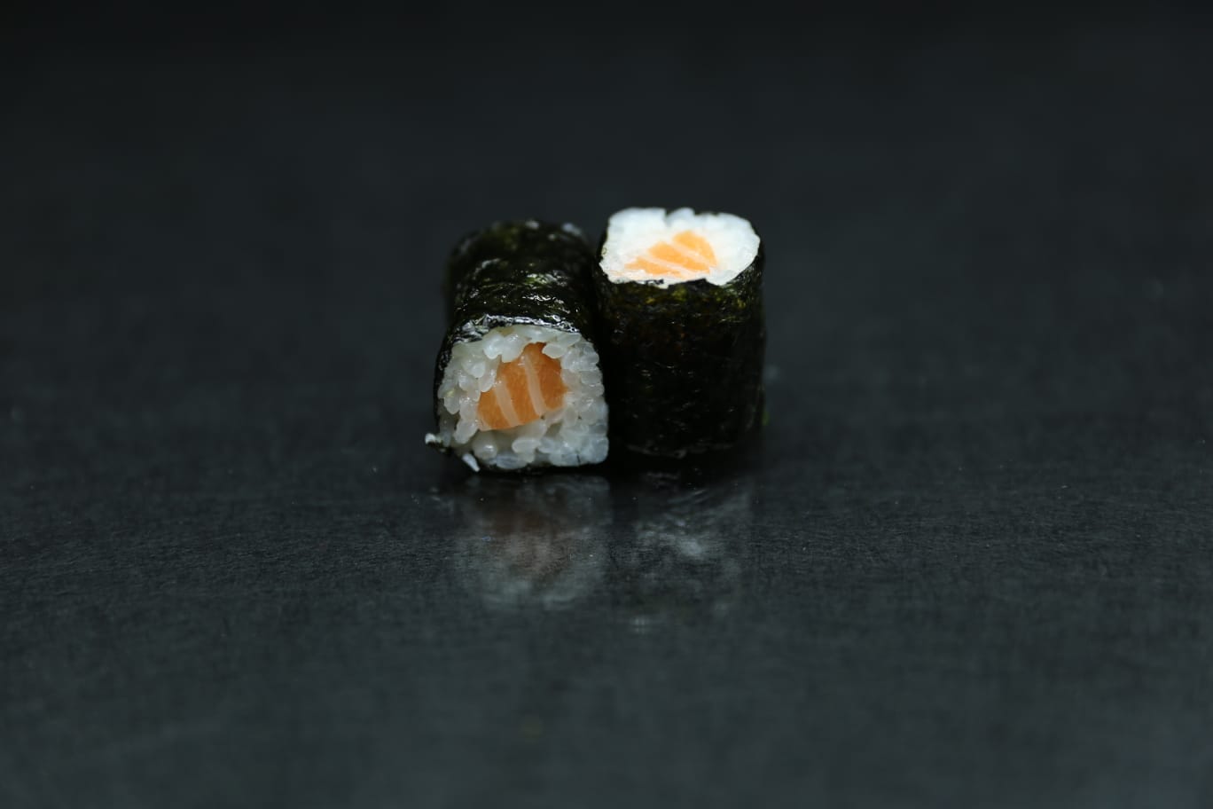 Due rotoli di sushi su una superficie scura, uno dei quali con ripieno di salmone.