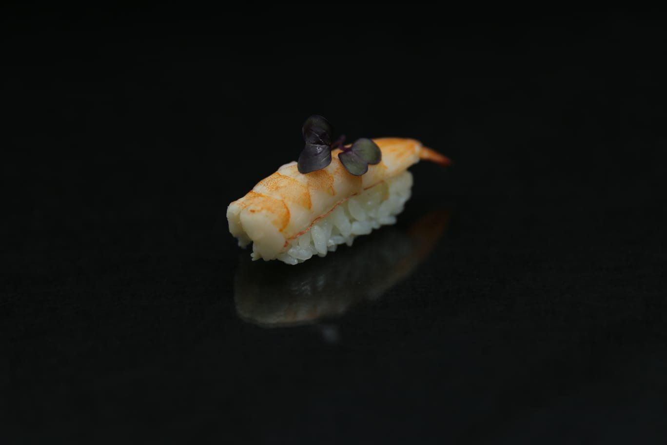 Un pezzo di sushi nigiri sormontato da due perle di caviale nero su sfondo scuro.