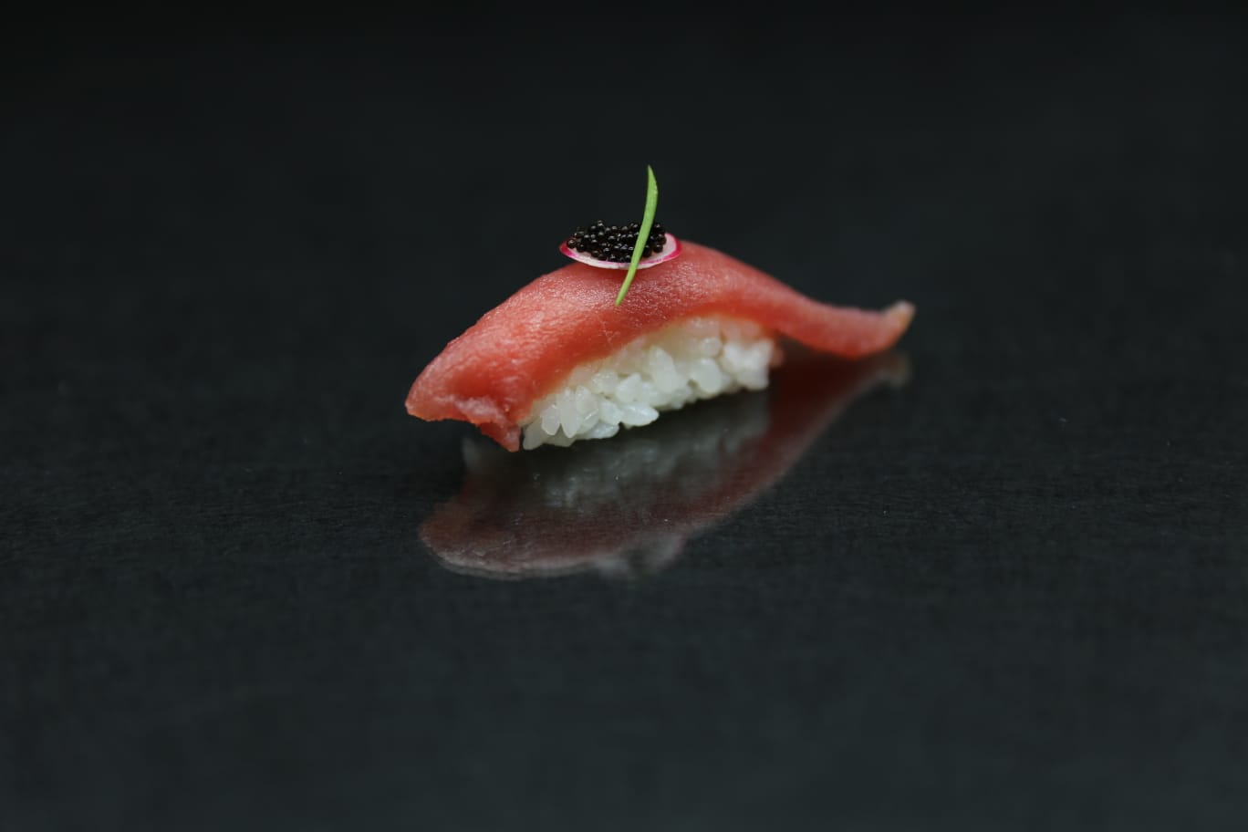 Sushi nigiri con pesce rosa su una superficie nera lucida, guarnito con una decorazione verde.
