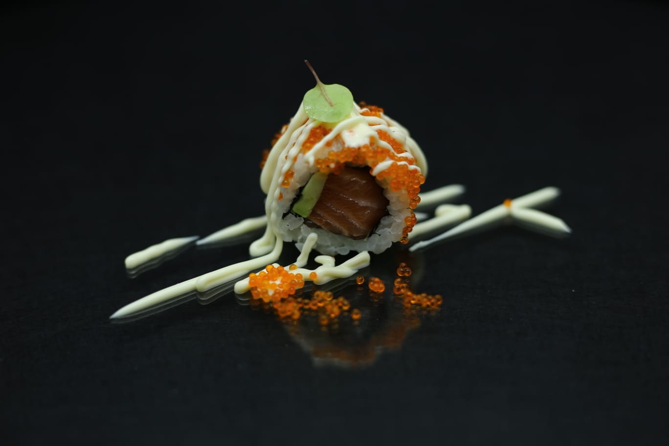Sushi roll con salsa all'arancia e guarnizione bianca su una superficie nera, decorato con una foglia di menta e bacchette.