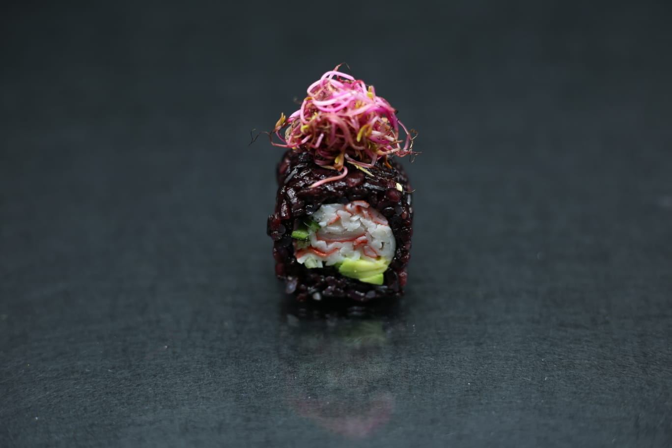 Un singolo rotolo di sushi con guarnizione rosa, centrato su uno sfondo scuro.