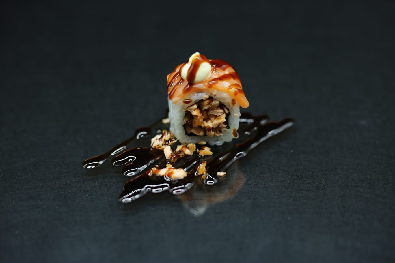 Sushi roll con salsa scura a filo su un piatto nero, guarnito con salsa arancione e decorazione