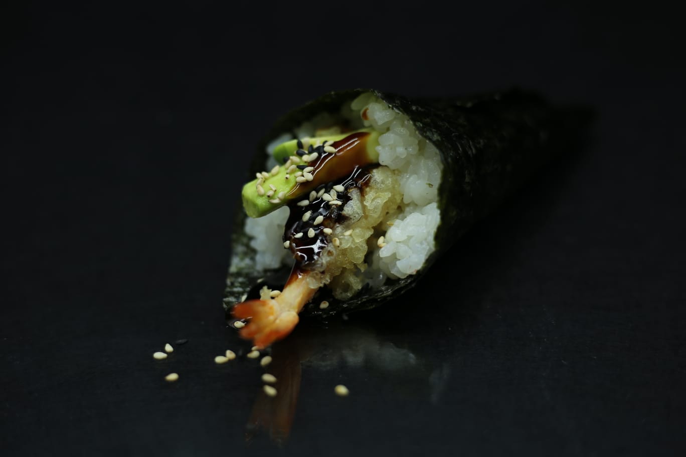 Un rotolo di sushi con riso, alghe, avocado e salsa su sfondo scuro