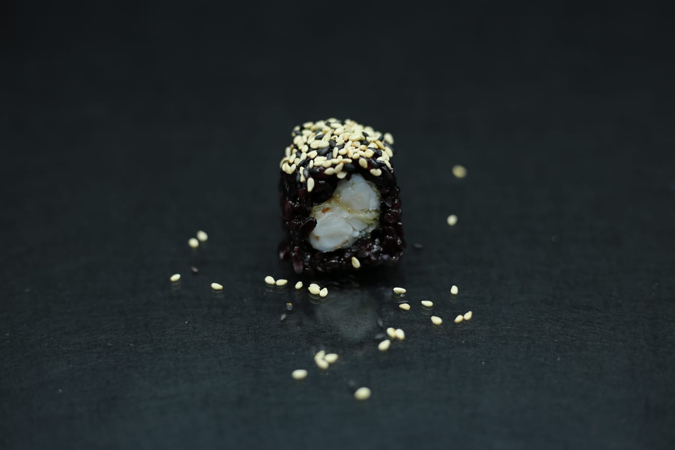 Piccolo dessert scuro guarnito con frutta secca tritata su uno sfondo scuro, con briciole sparse nelle vicinanze.