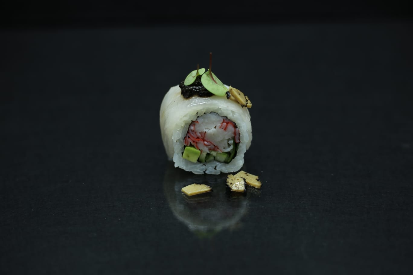 Rotolo di sushi con riso bianco, avocado e ripieno rosso su sfondo scuro