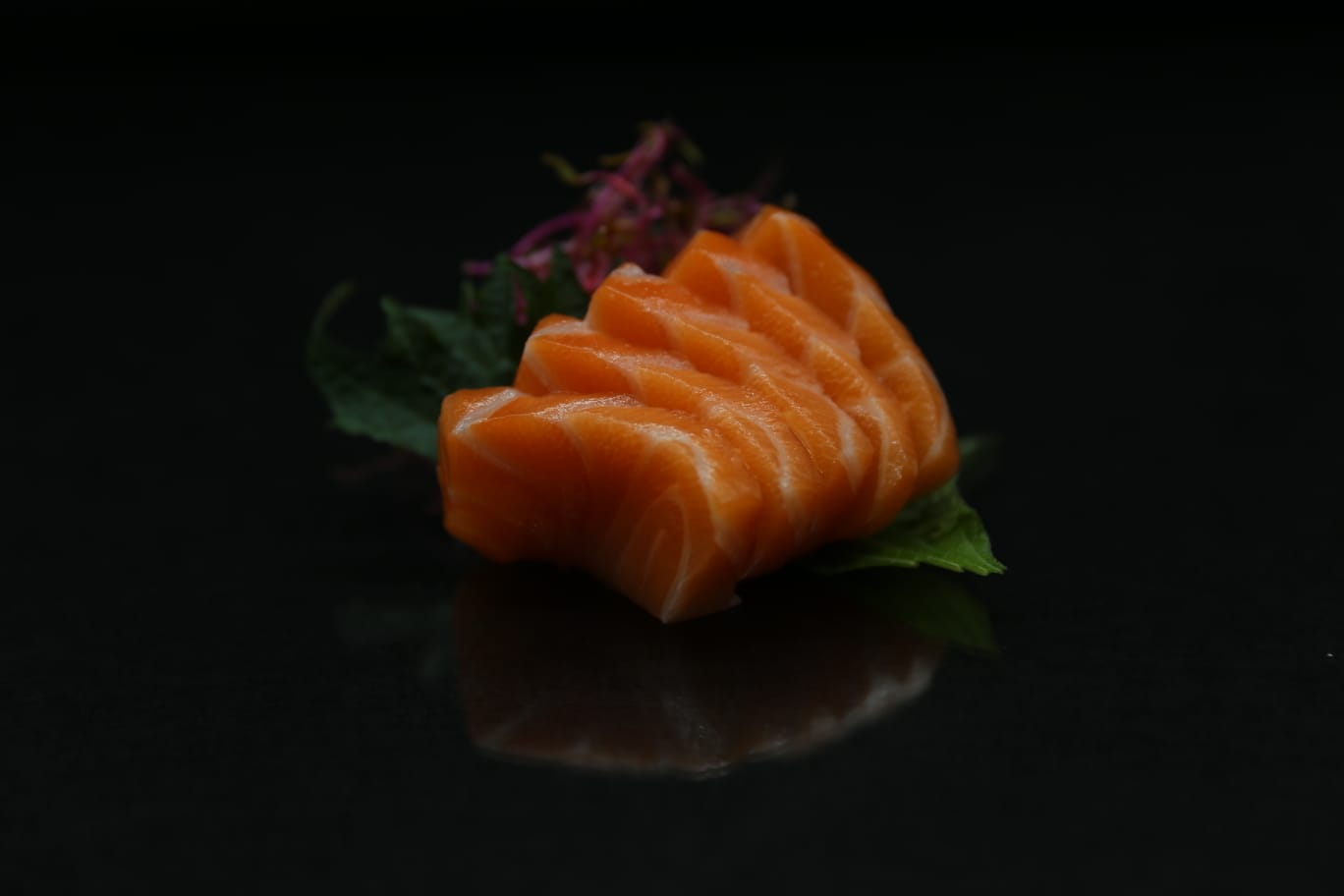Fette di sashimi di salmone su un piatto scuro con guarnizione