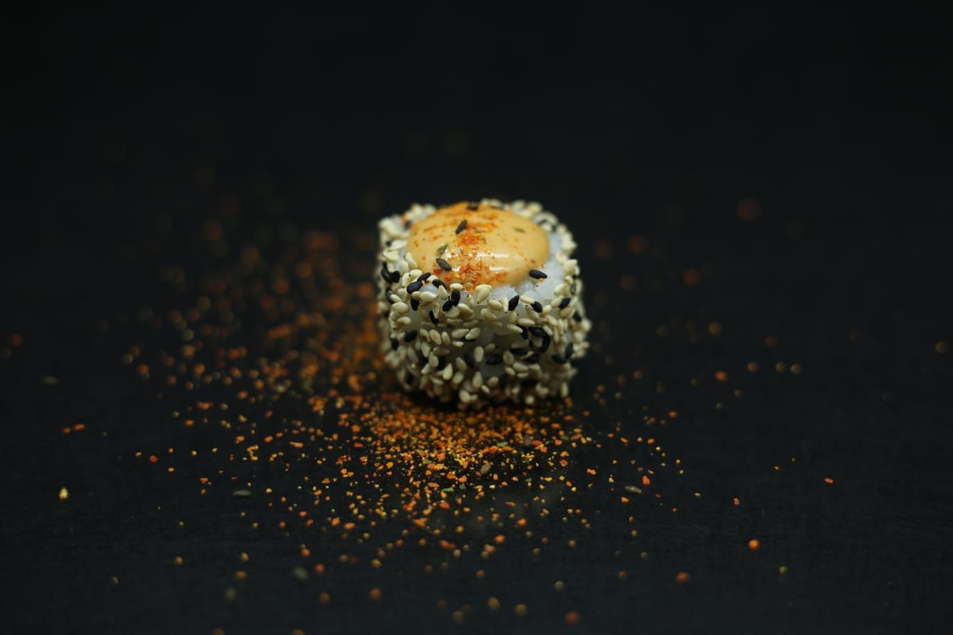 Rotolo di sushi con salmone su una superficie scura, cosparso di fiocchi di condimento arancione.