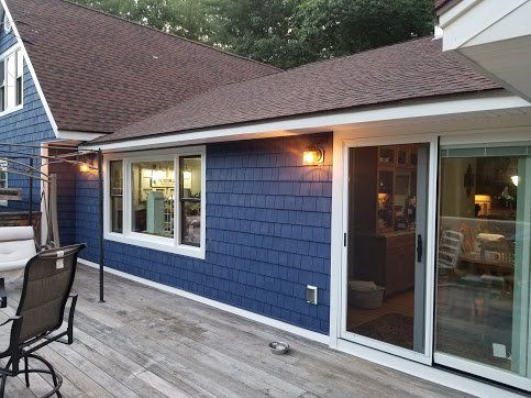 Blue-shingled home exterior with a wooden deck, a sliding glass door, and a white-framed window at sunset.