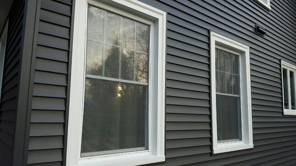Two white-framed windows on the exterior of a house with dark gray horizontal siding.