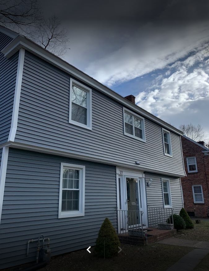 A two-story blue-sided house with white trim and windows under a cloudy sky.