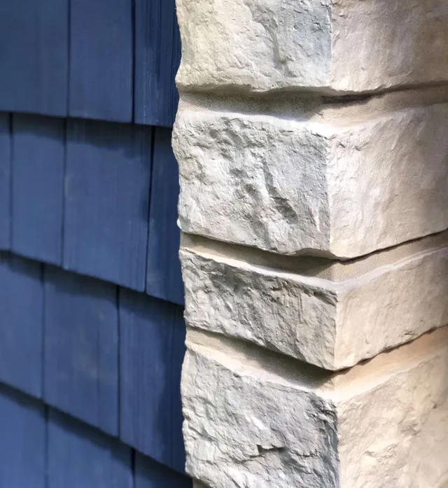 A close-up of a blue shingled wall meeting a light-colored, stacked stone corner column.