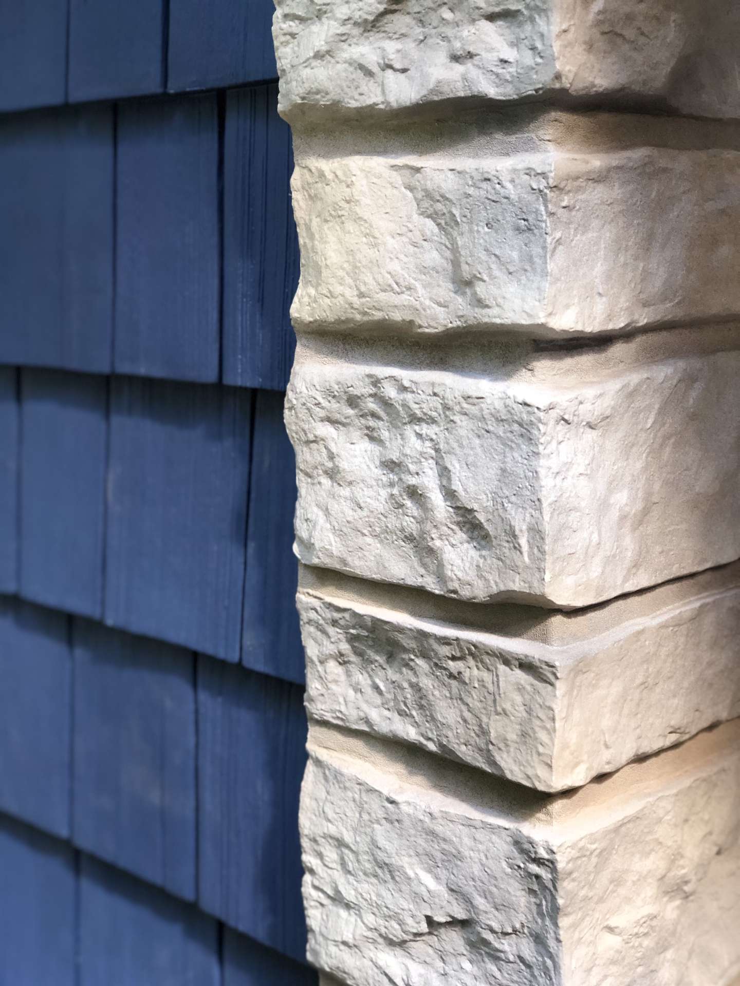 A close-up view showing the contrast between blue wooden shingles and light-colored, rough-cut stone wall cladding.