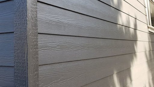 Gray fiber cement siding panels with a wood grain texture meeting at a corner trim piece.