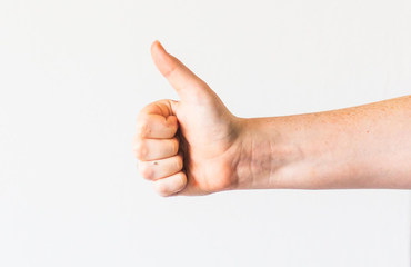 A person’s hand against a white background, making a thumbs-up gesture.