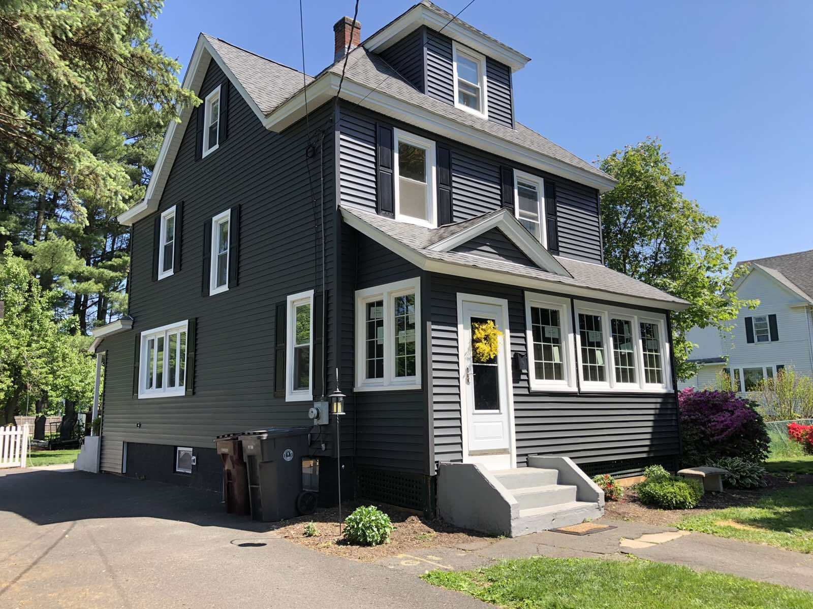 A two-story house with dark gray siding, white trim, and an attached front porch under a sunny blue sky.