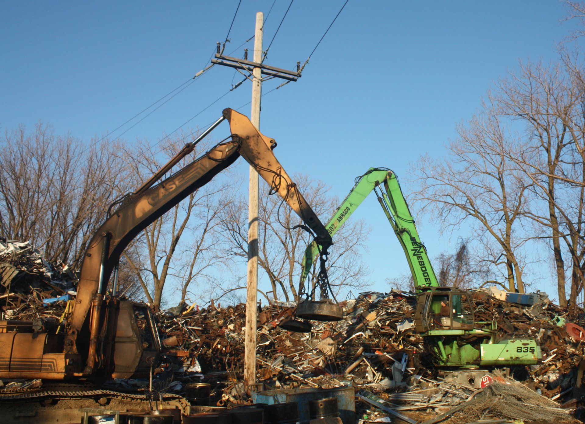 Two excavators are working on a pile of scrap metal