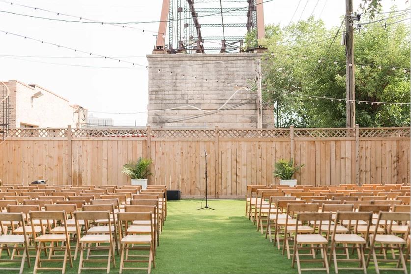 A row of wooden folding chairs are lined up in front of a wooden fence.