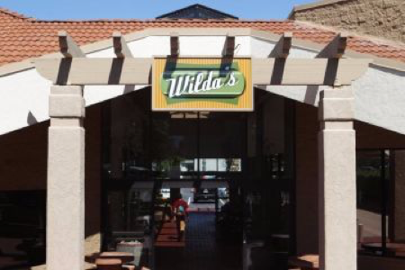 Restaurant 'Wilda's' with bold green/yellow sign, framed by stucco archway, beige pillars under clear blue sky.