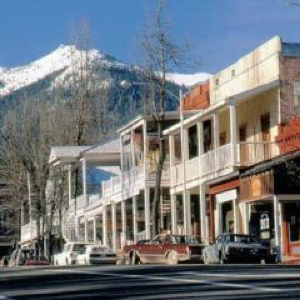 Picturesque street view with two-story buildings, balconies, old-fashioned architecture, and snow-capped mountains.