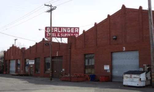 Red brick industrial building with garage doors, large sign 'Gerlinger Steel & Supply Co,' clear blue sky.