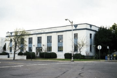 White art deco-style building with 'Postal Telegraph Cable' engraved facade, beside empty street, overcast skies.