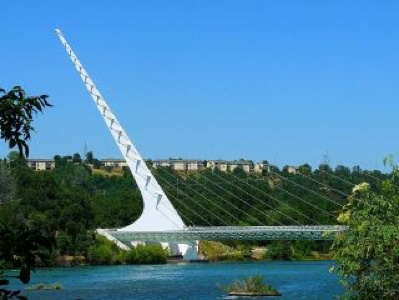 Modern white cable-stayed bridge with tall pylon over tranquil
river, lush greenery, clear sky. Sundial Bridge, Redding. CA.