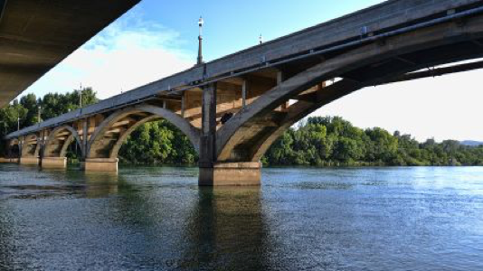 Concrete arched bridge over tranquil river, lush greenery, clear blue sky. Diestlehorst Bridge. Redding, CA.