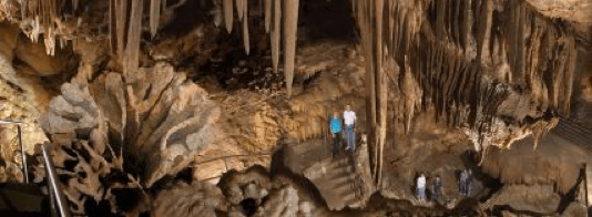 People exploring cave with stalactites, flowstone formations, illuminated by artificial lighting - Shasta Caverns
