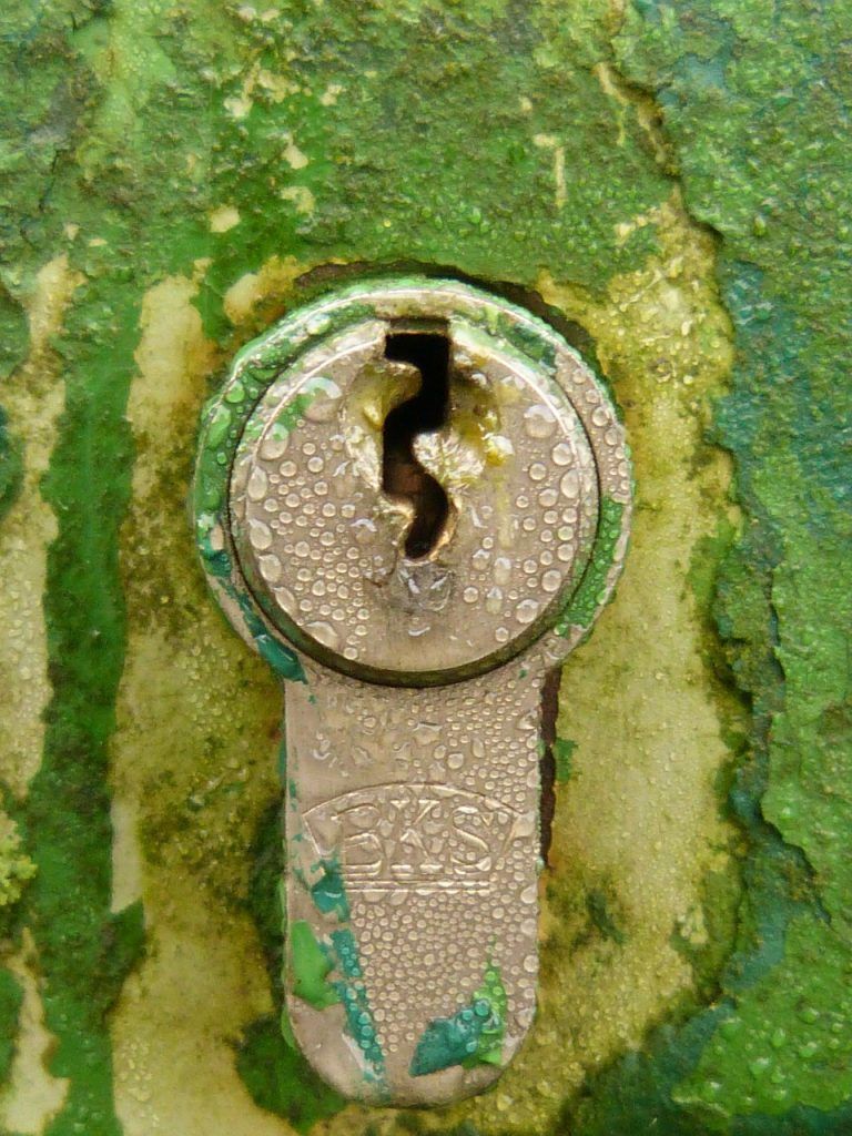 Close-up of a weathered key in a corroded lock, highlighting intricate details and textures, on a greenish surface.