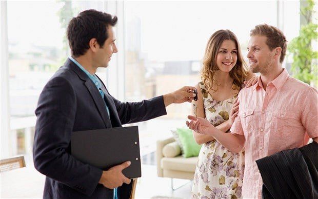 A Property Manager giving keys to happy couple in bright home interior, symbolizing new home purchase.
