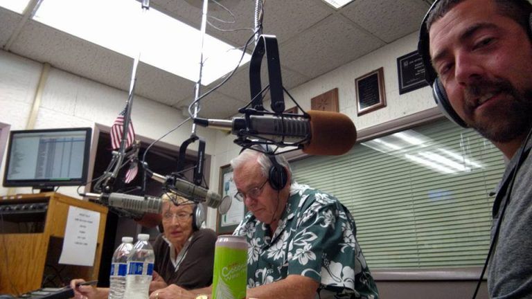 Three individuals in radio studio: one takes selfie, others focus on broadcast.