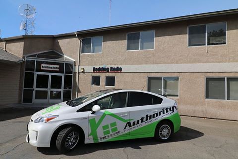 A branded white and green 'Authority' car parked in front of 'Redding Radio' building.
