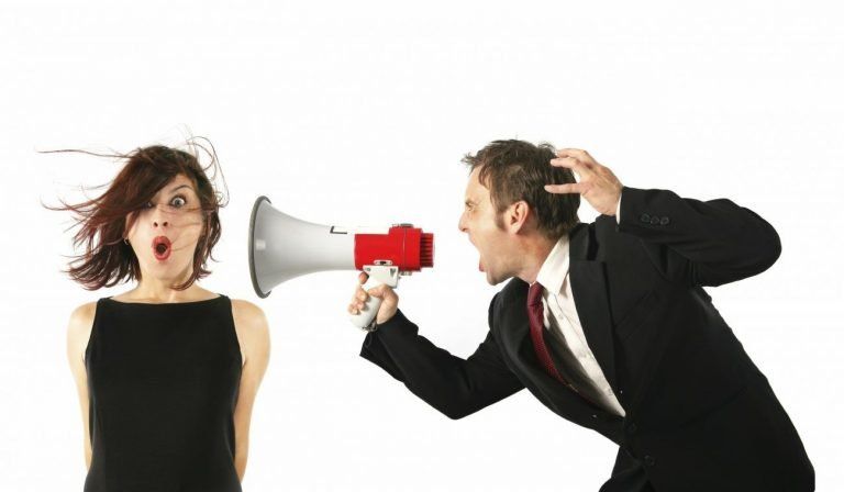Man in suit using megaphone near surprised woman's ear, her hair blown back by the sound.