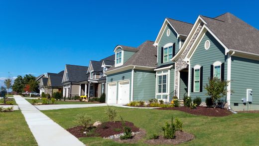 A row of green and white houses with a sidewalk in front of them.