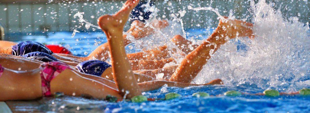 Swimmers in a blue pool, splashing water. Legs and swimwear visible.