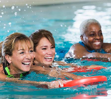 Three women in a pool doing water aerobics, smiling.