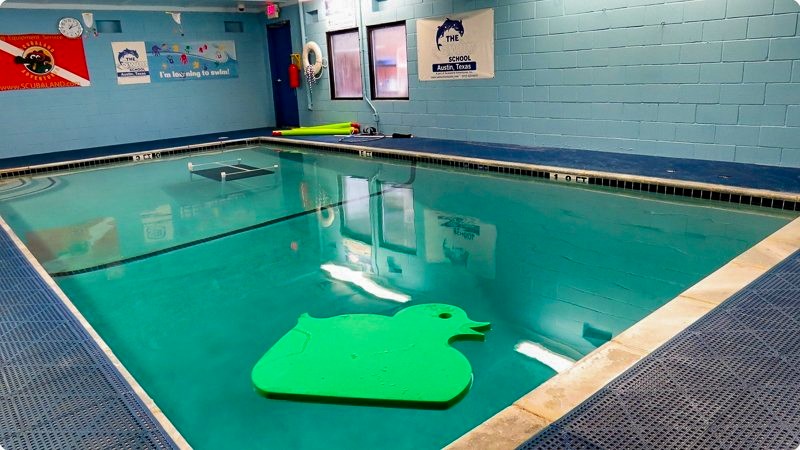 Indoor swimming pool with turquoise water, a large green duck-shaped float, and blue walls.