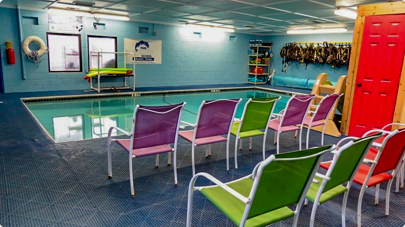 Indoor swimming pool with colorful chairs, likely for lessons or observation.