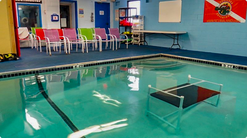 Pool with platform, chairs, and flag. An underwater figure appears to be swimming.