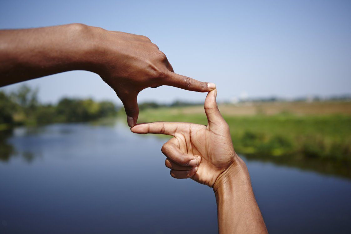 Handen omlijsten een vergezicht over een kalme rivier onder een blauwe hemel.